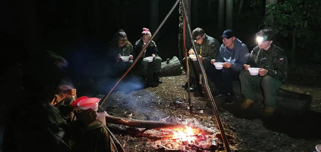 Uczniowie nocą jedzący przy ognisku